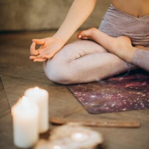 A woman practicing yoga indoors in lotus pose with candles creating a calming atmosphere.