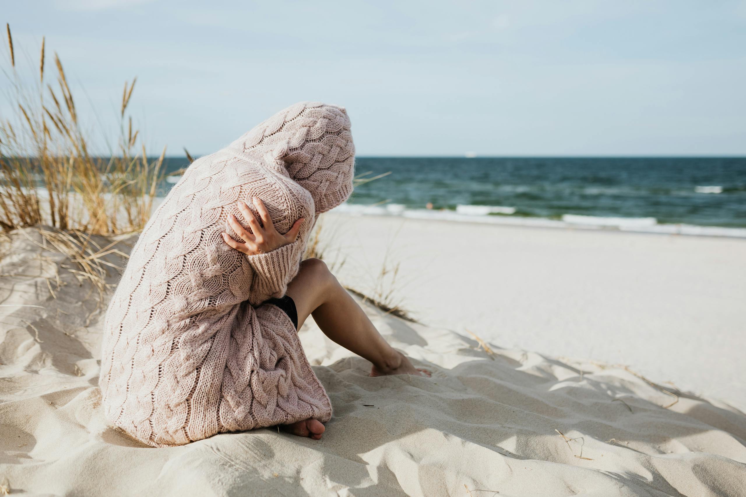 Solitary woman in pink knitted sweater on a tranquil beach setting.