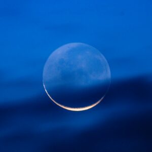 Stunning view of a crescent moon glowing in a deep blue night sky with dark clouds.