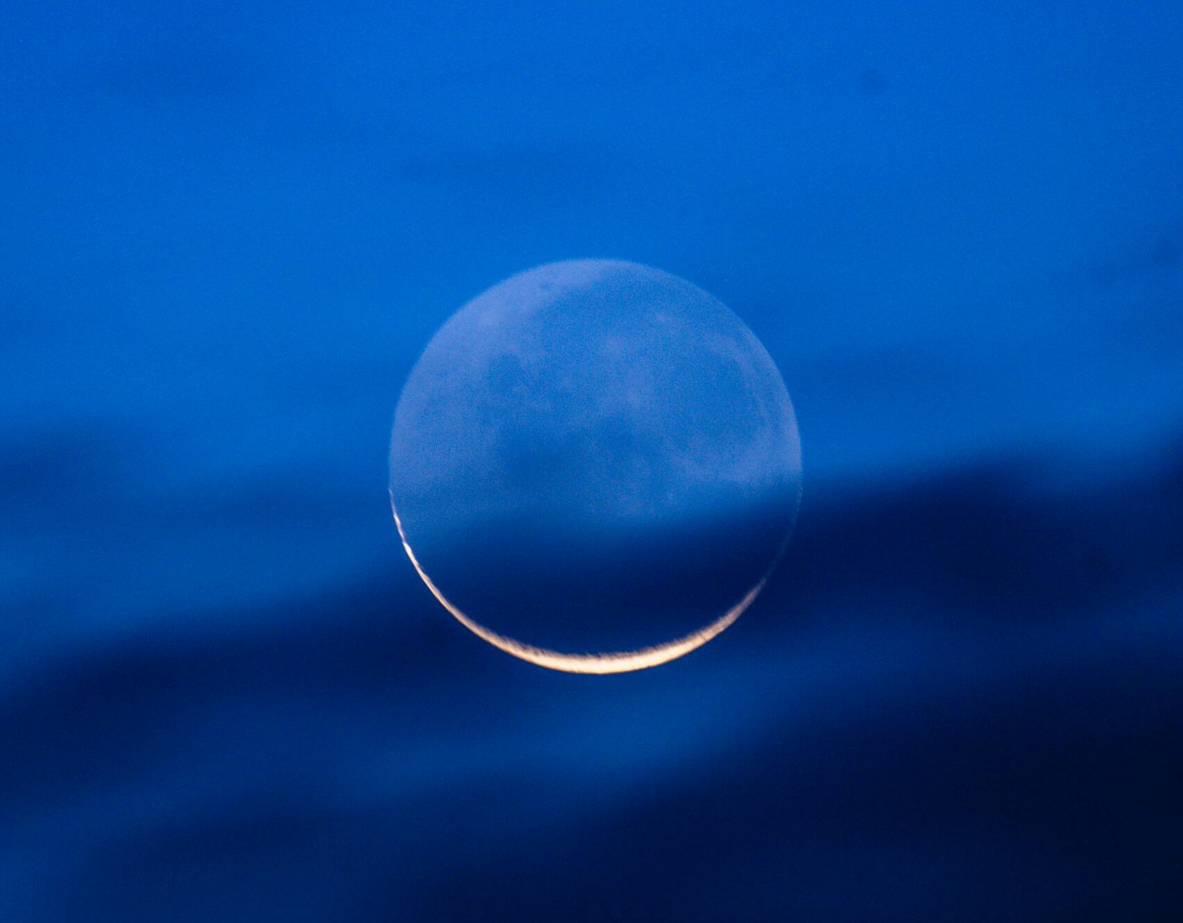 Stunning view of a crescent moon glowing in a deep blue night sky with dark clouds.